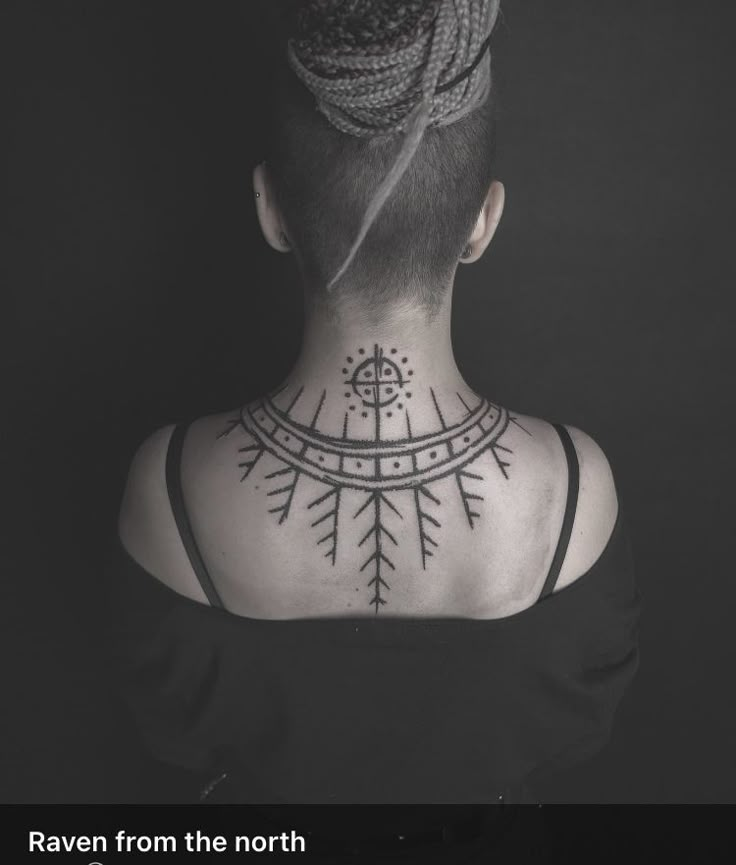 the back of a woman's neck with an intricate tattoo design on her left shoulder