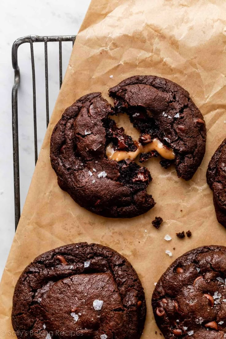 four chocolate cookies are on a piece of parchment paper