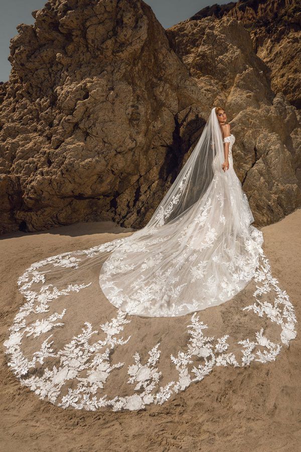 a woman in a wedding dress standing on the beach with her veil blowing in the wind