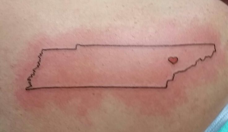 a small tattoo on the back of a woman's shoulder with a heart in it