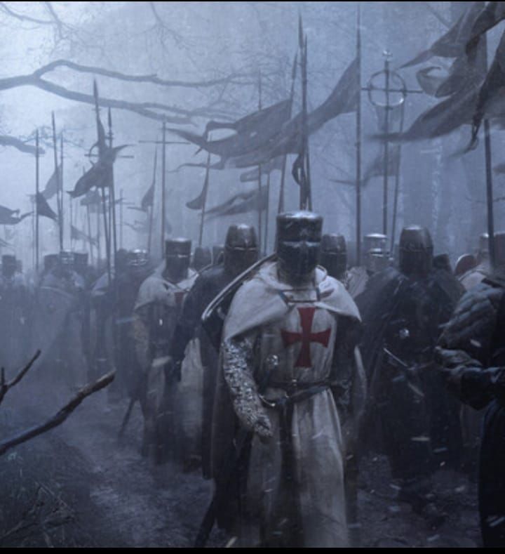 a group of men dressed in medieval armor walking through the woods with flags behind them