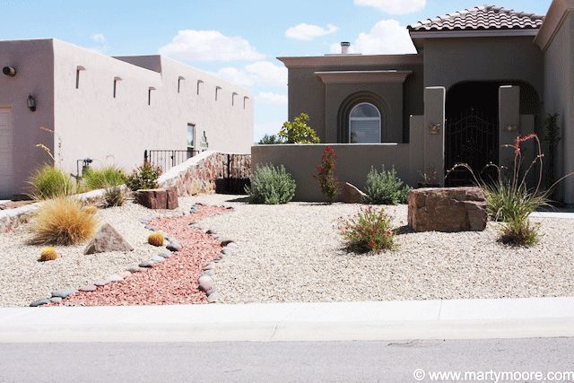 a house in the desert with rocks and plants on the front lawn, along with other houses