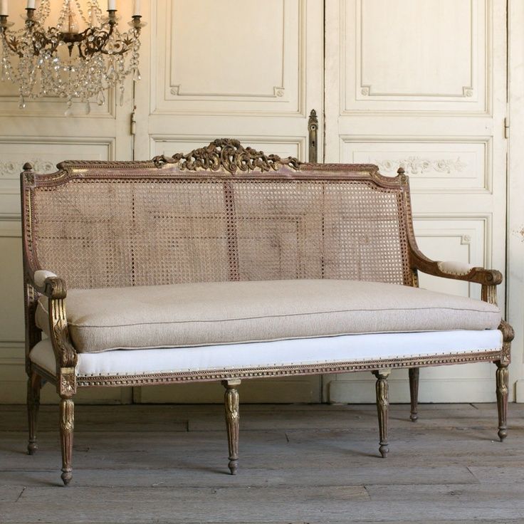 an antique style couch with white cushions and gold trimmings, in front of a chandelier