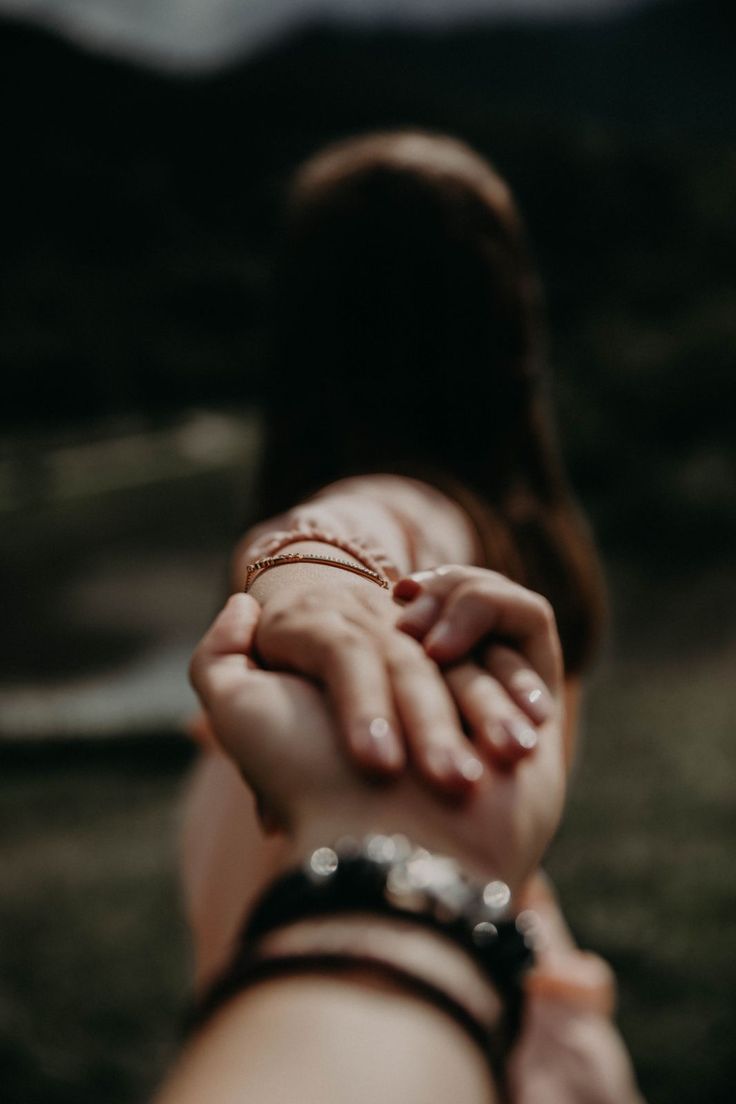 two hands holding each other in the middle of a field with mountains in the background