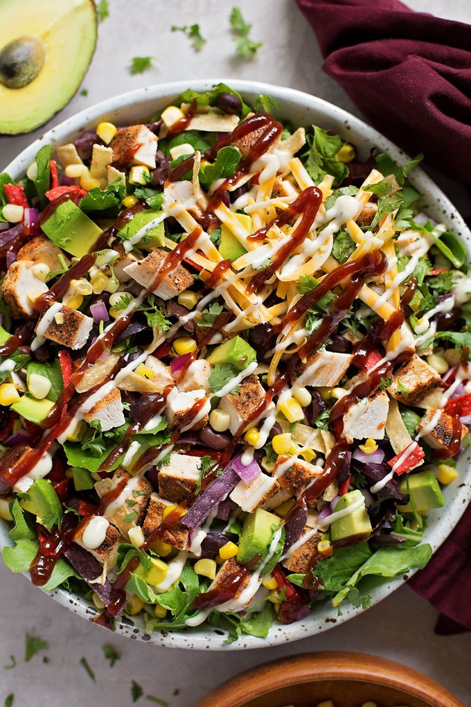 a salad with chicken, lettuce, corn and dressing in a bowl next to an avocado