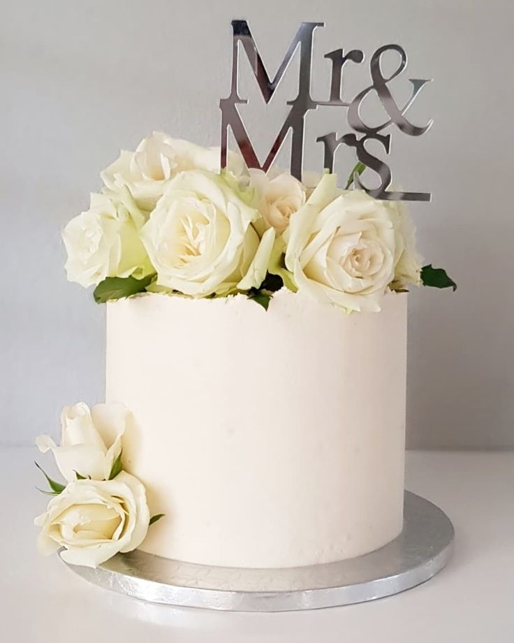 a wedding cake with white roses and mr and mrs topper on the bottom tier