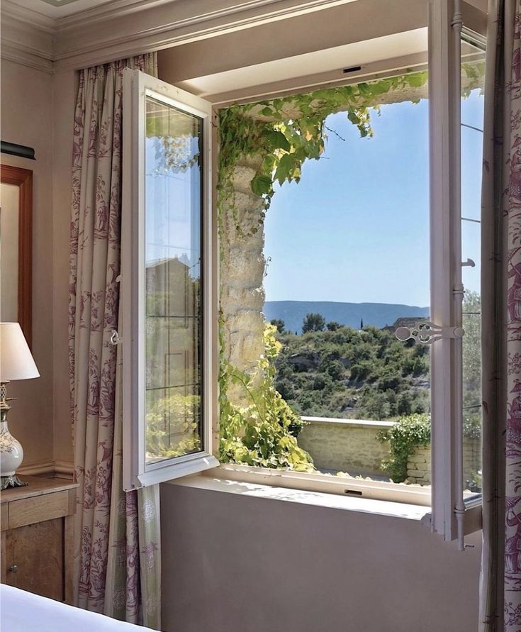 a bedroom with an open window looking out onto the ocean and trees outside, in front of a white bed