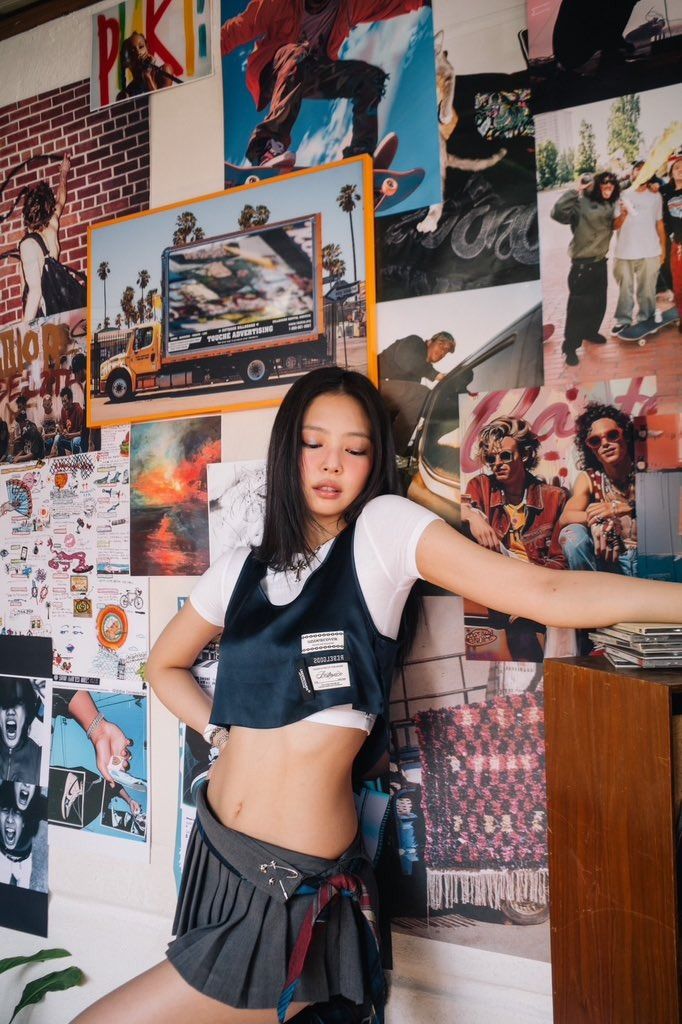 a young woman posing in front of a wall covered with pictures and posters, holding her leg up