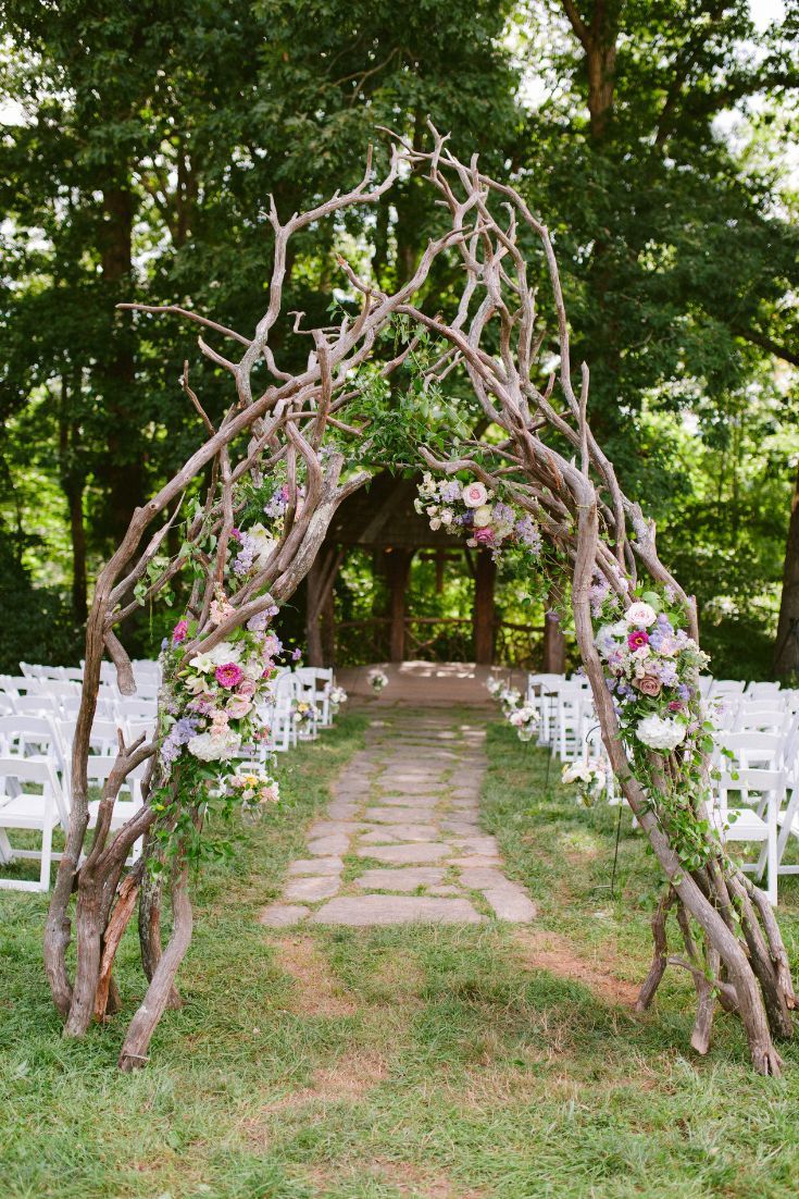 an arch made out of branches with flowers and greenery at the end is decorated with white chairs