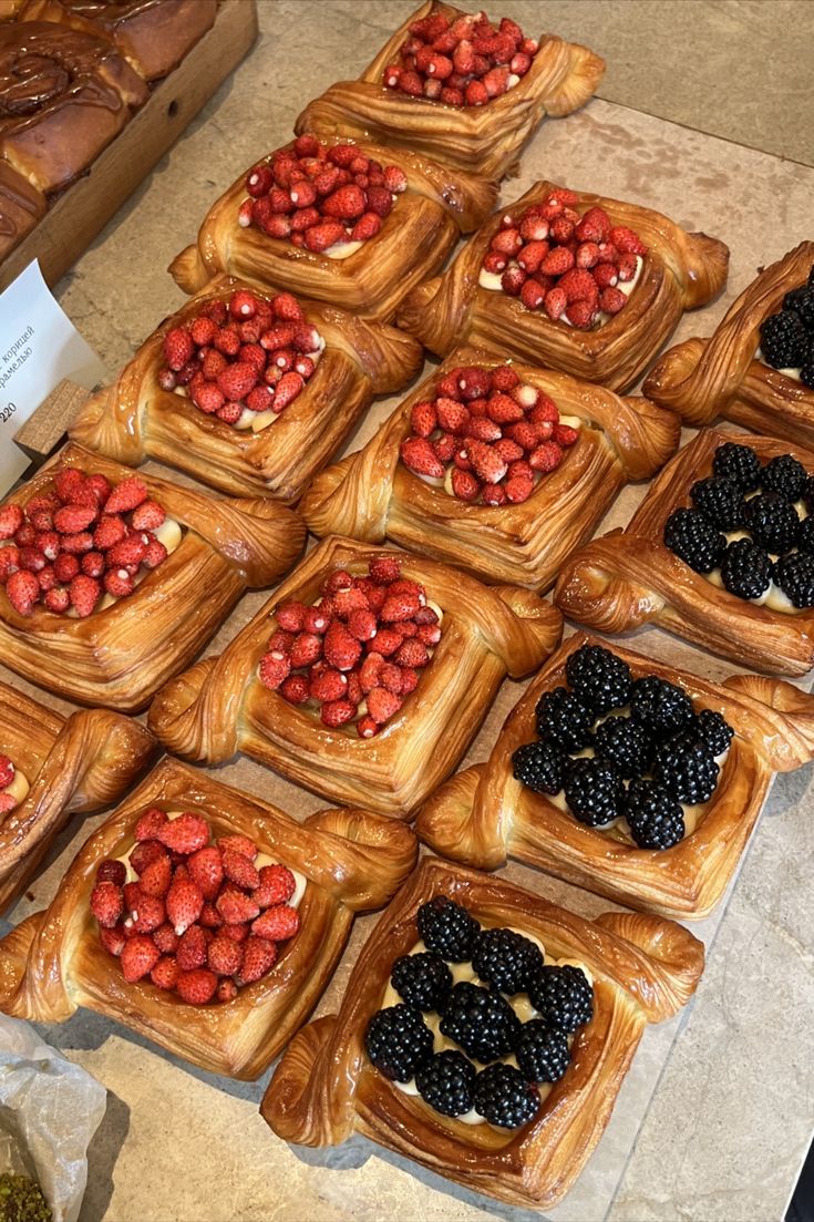 many different types of pastries on display in a bakery case, including raspberries and blackberries