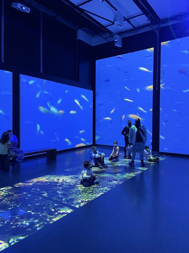 people are standing in front of an aquarium looking at the fish and other things on display