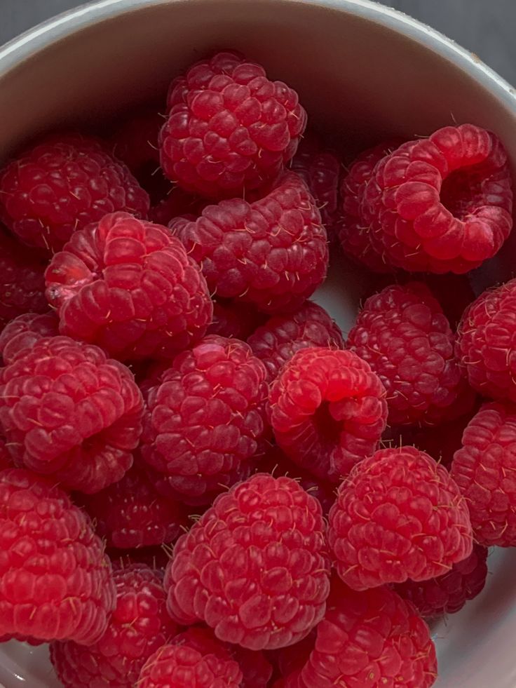 fresh raspberries in a white bowl on a gray table top, ready to be eaten