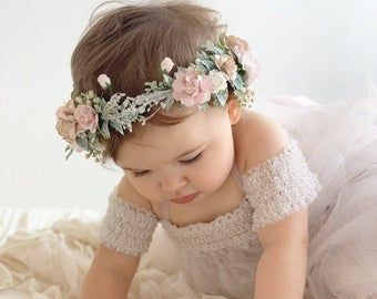 a baby girl wearing a flower crown on top of a white blanket with her hands in her face