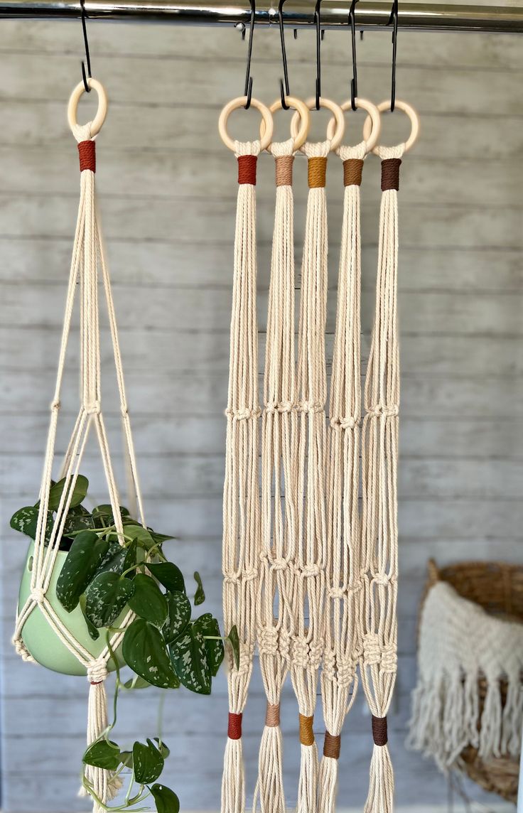 macrame plant hangers with wooden handles and hooks hanging from the ceiling next to a potted plant