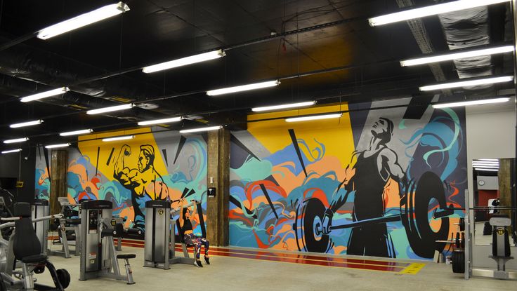 an indoor gym with colorful graffiti on the wall and exercise machines in the foreground