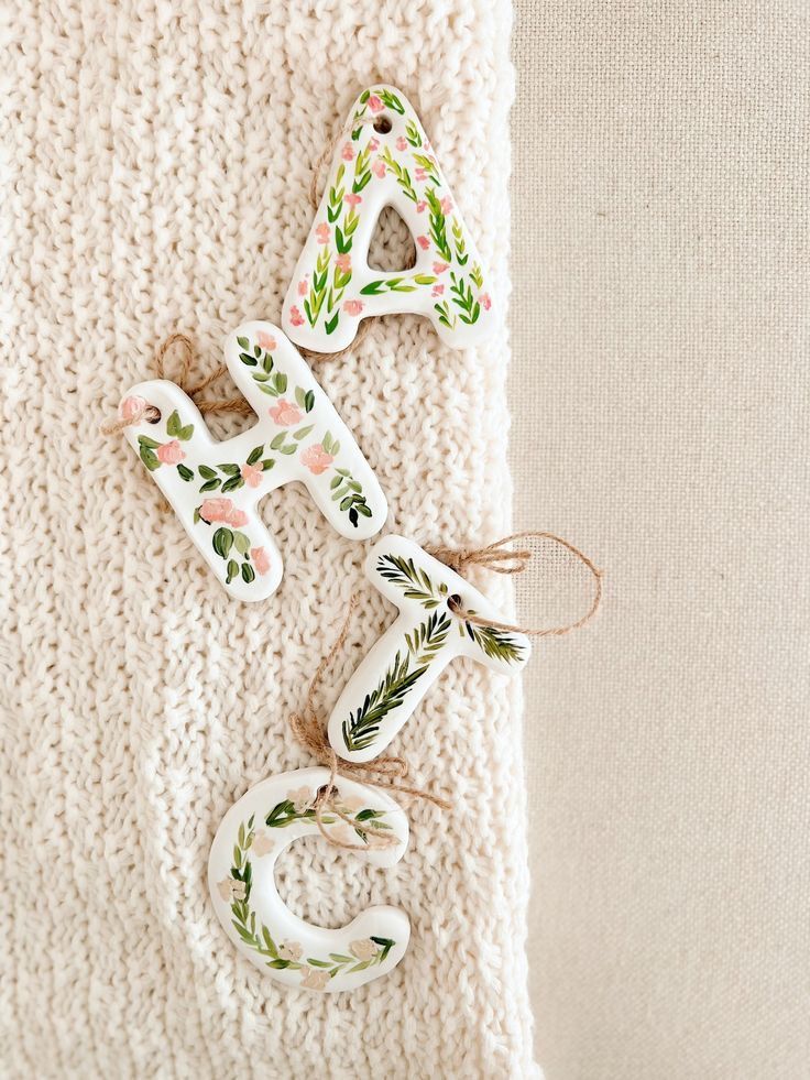 three ceramic ornaments are hanging on a white blanket, one is decorated with leaves and the other has an ornament