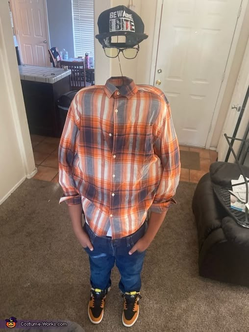 a young boy standing in front of a door wearing an orange and blue plaid shirt