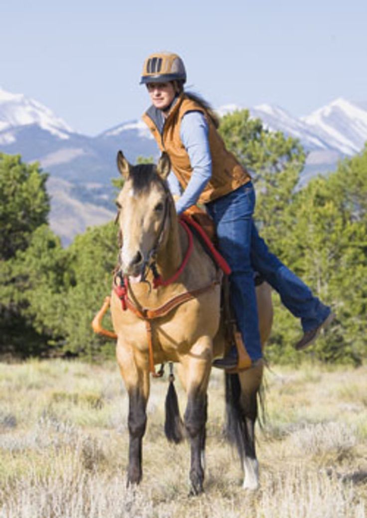 a woman riding on the back of a brown horse in a field with mountains in the background