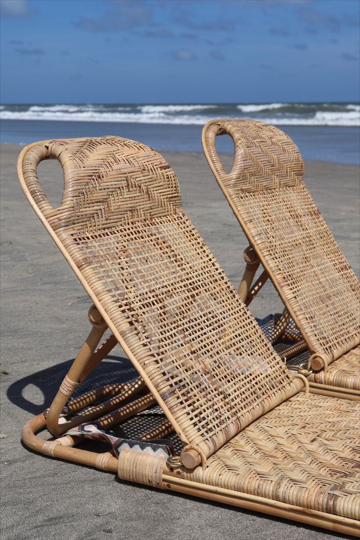 two wicker lounge chairs sitting on the beach