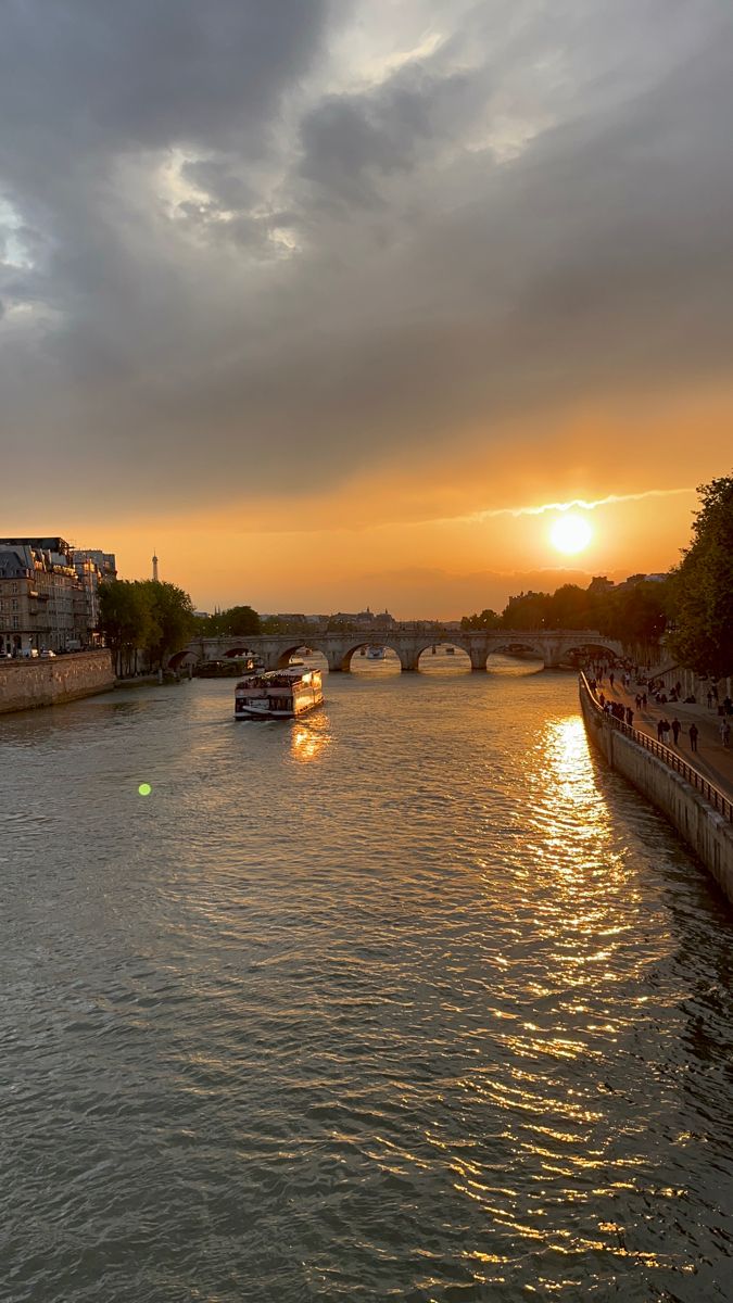 the sun is setting over the river with boats on it