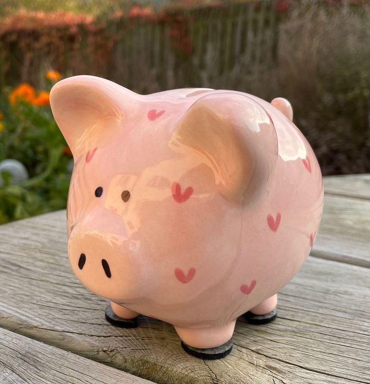 a pink piggy bank sitting on top of a wooden table next to some flowers