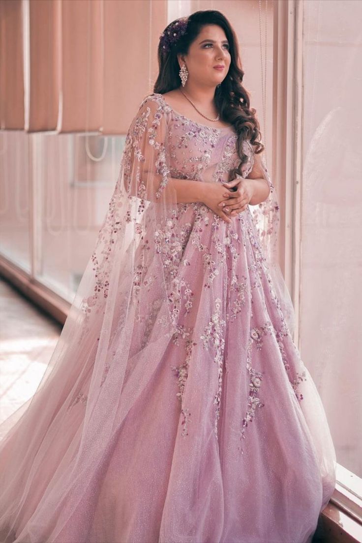 a woman in a pink gown standing by a window with her hands on her hips