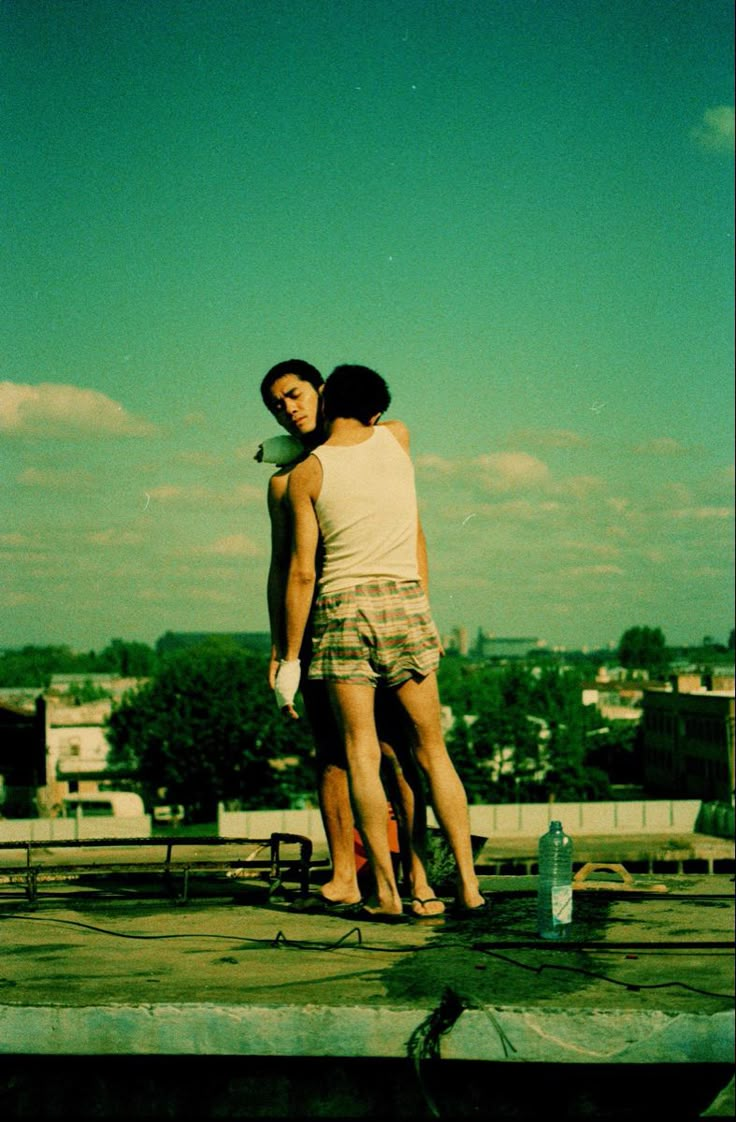 two people standing on top of a roof with their arms around each other's shoulders