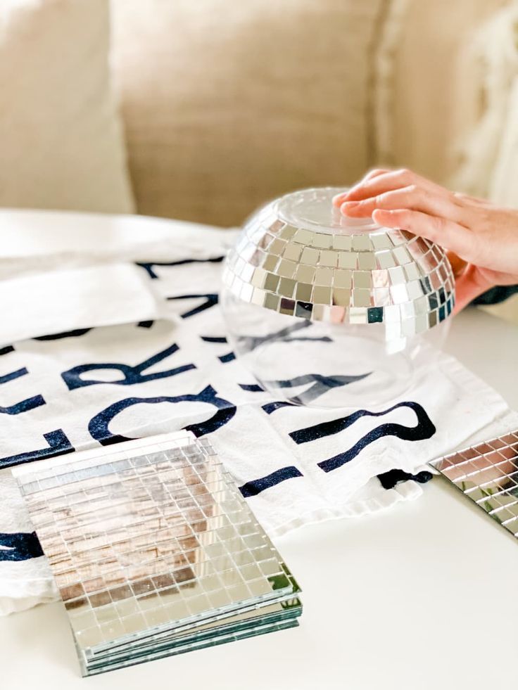 a person holding a disco ball on top of a white table next to some mirrors