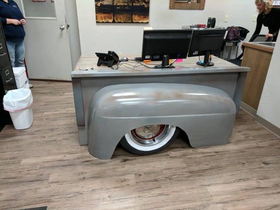 an old car shaped desk in the middle of a room with people working on computers