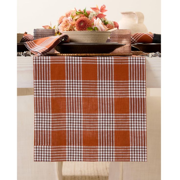 an orange and white checkered table runner on a dining room table with flowers in a vase