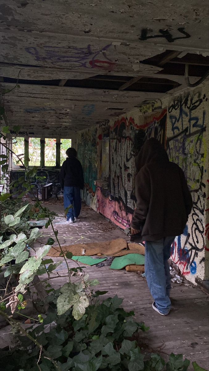 two people walking in an abandoned building with graffiti on the walls