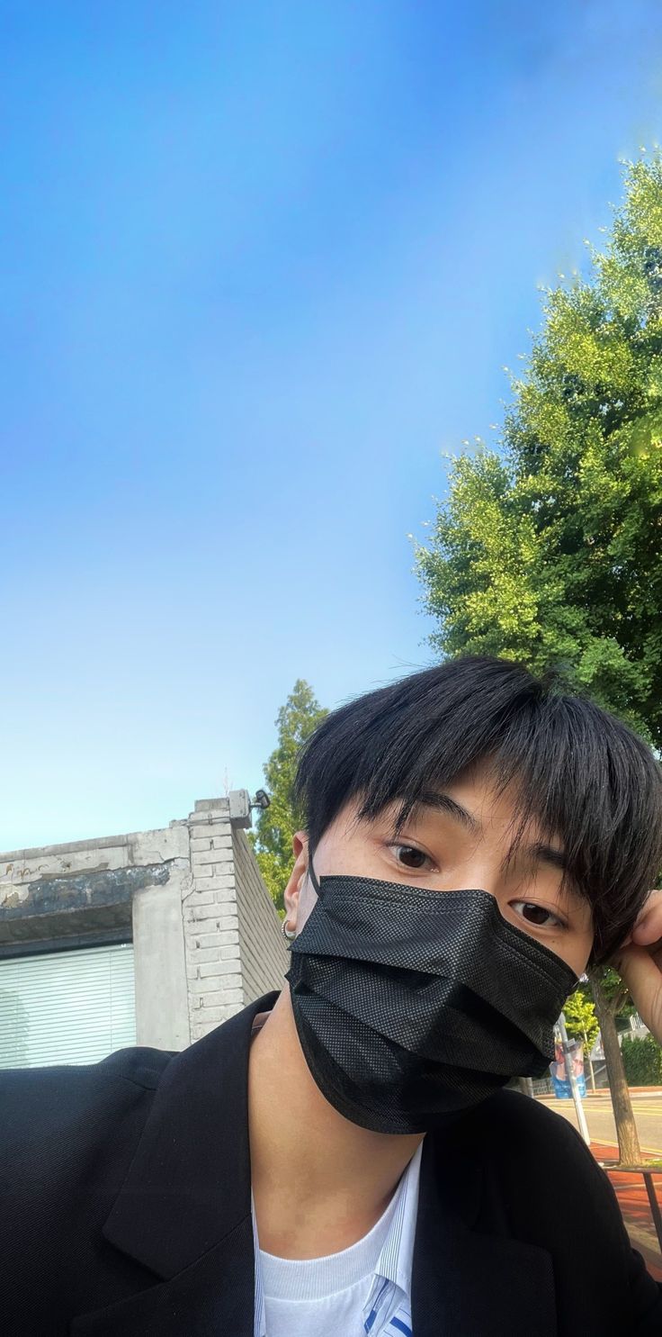 a young man wearing a black mask with trees in the back ground and blue sky behind him