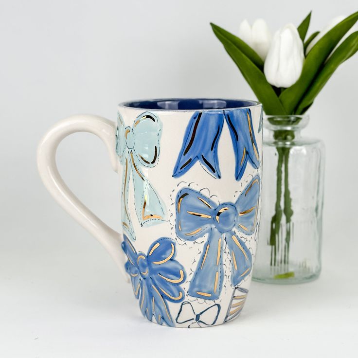 a blue and white coffee mug next to a vase with tulips in it