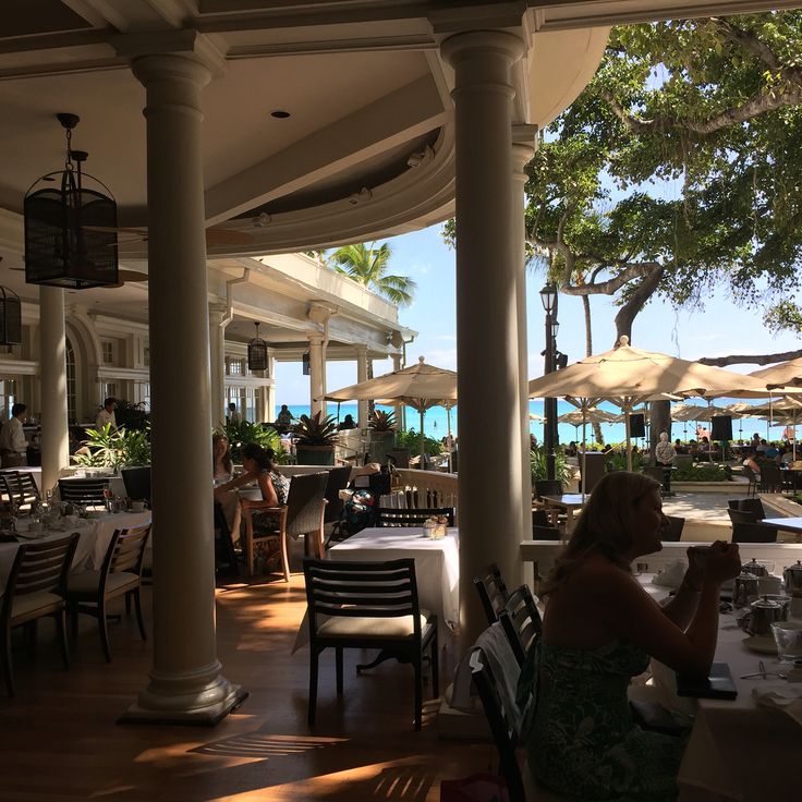 a woman sitting at a table in front of an outdoor restaurant with tables and umbrellas