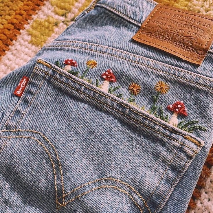 a pair of jeans with embroidered flowers and mushrooms on the back, sitting on a rug