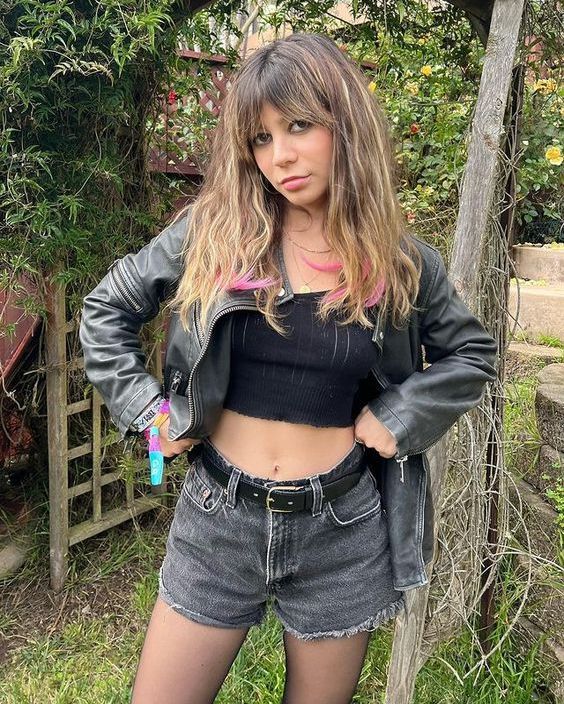 a woman in short shorts and a leather jacket posing for the camera with her hands on her hips