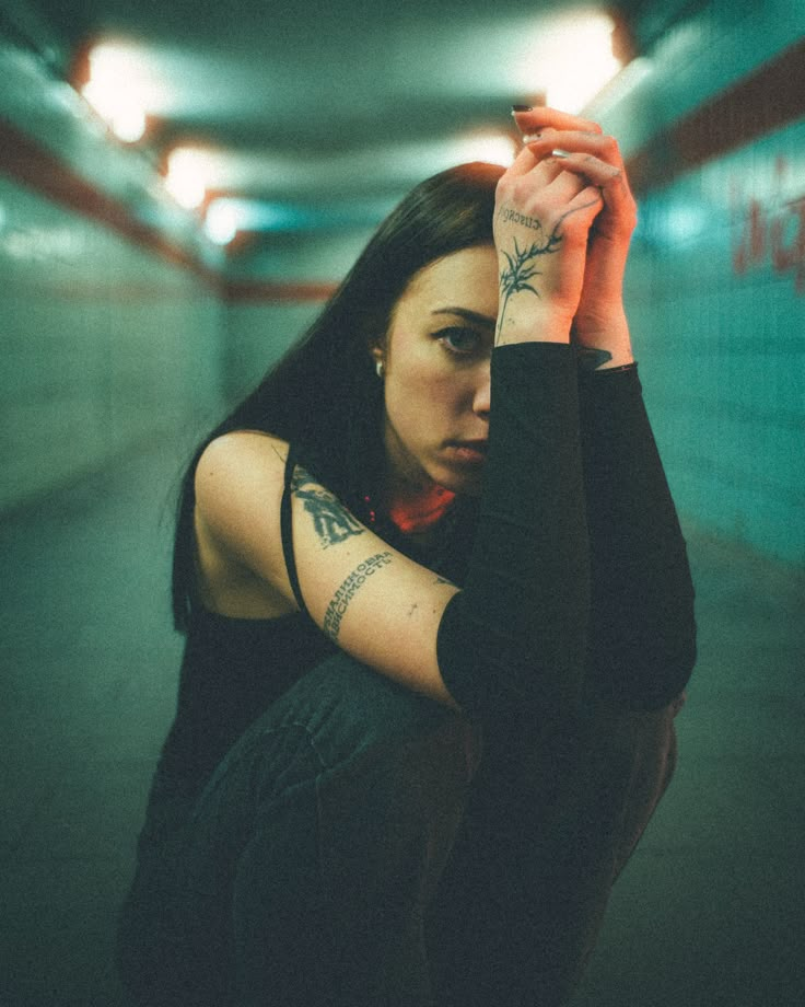 a woman sitting on the ground holding her hand up to her head and looking off into the distance