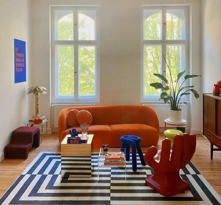 a living room filled with furniture next to two large windows on top of a hard wood floor