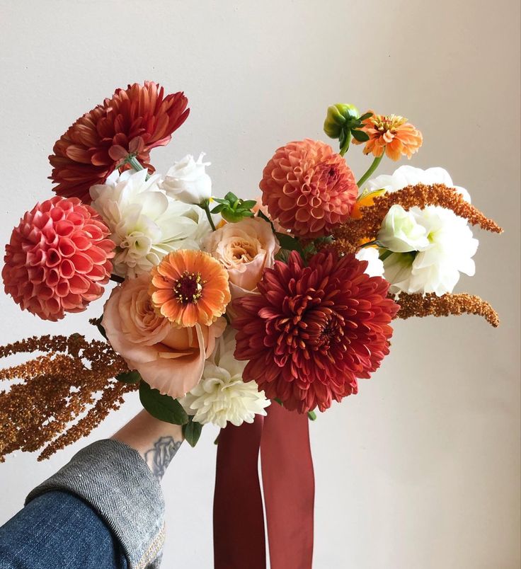 a vase filled with lots of flowers on top of a wooden table next to a person's leg