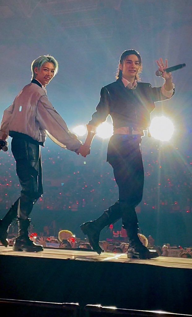 two men holding hands while walking on stage at a concert with lights in the background