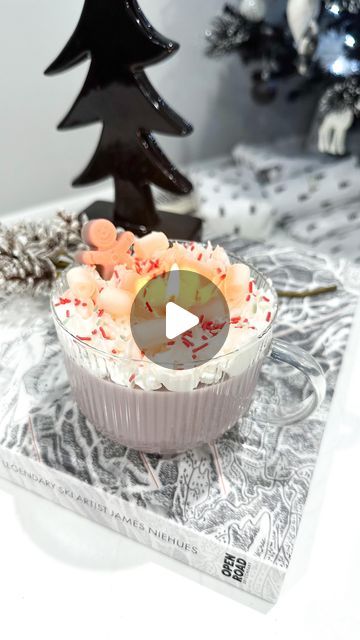 a cupcake with white frosting and sprinkles sits on a table next to a christmas tree