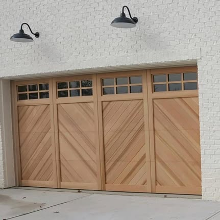 two lights on the side of a white brick building and a brown wooden garage door