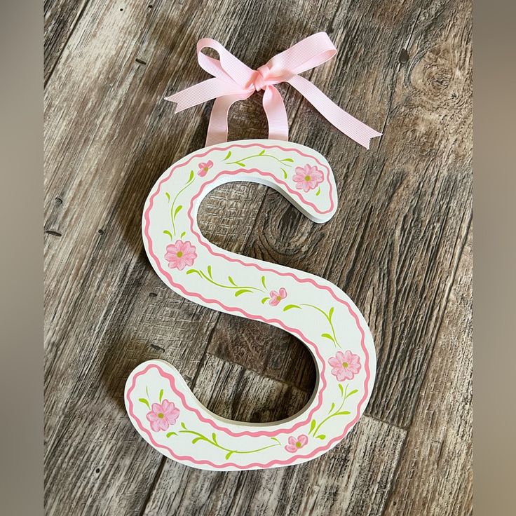 the letter s is decorated with flowers and pink ribbon on a wooden surface, next to a bow