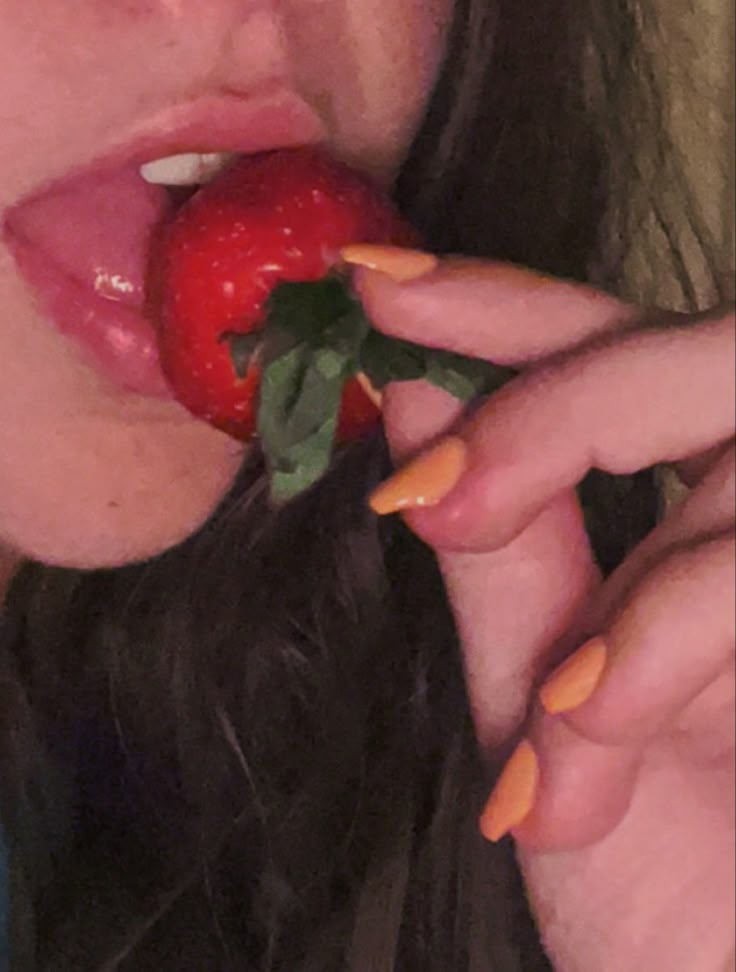 a woman eating an apple while wearing orange nails