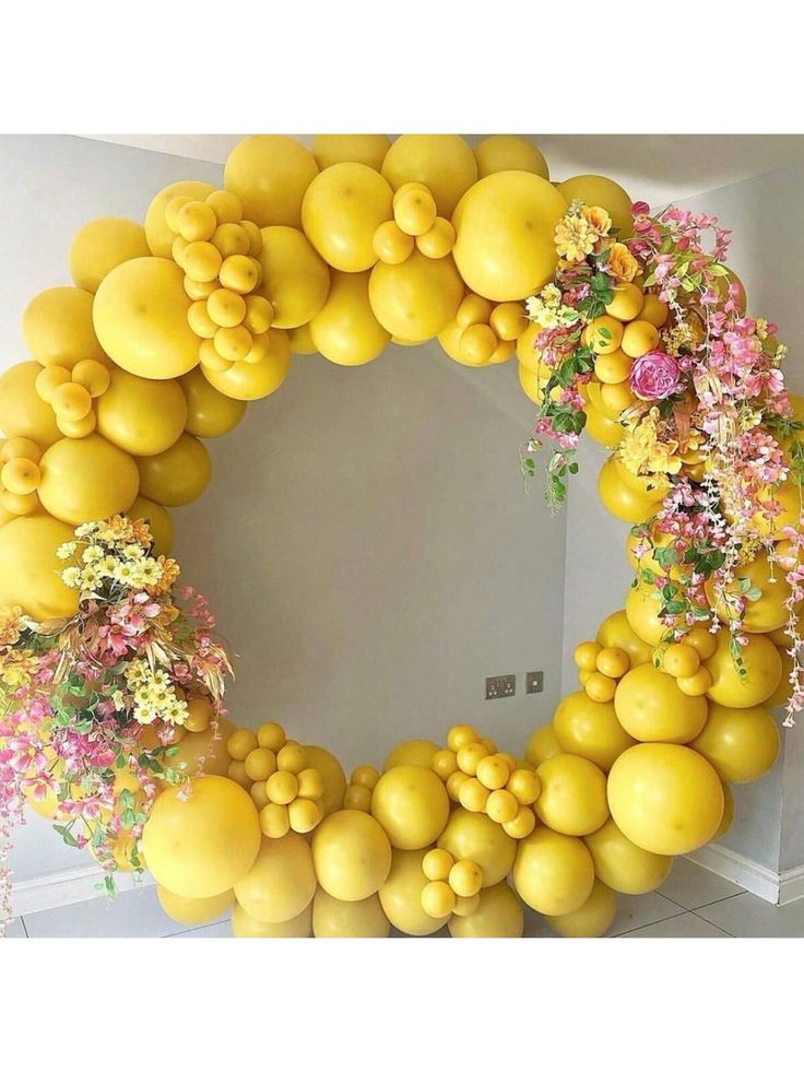 a wreath made out of yellow balloons and flowers on the front of a room with white walls