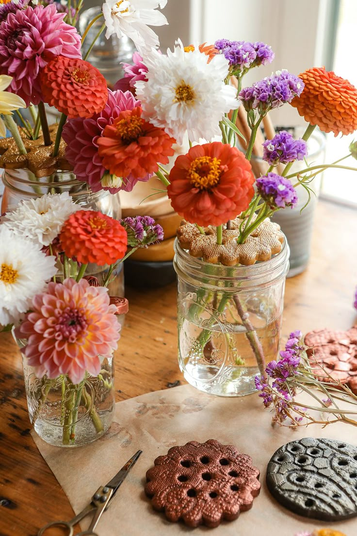 flowers in vases and cookies on a table next to cookie cutters with scissors