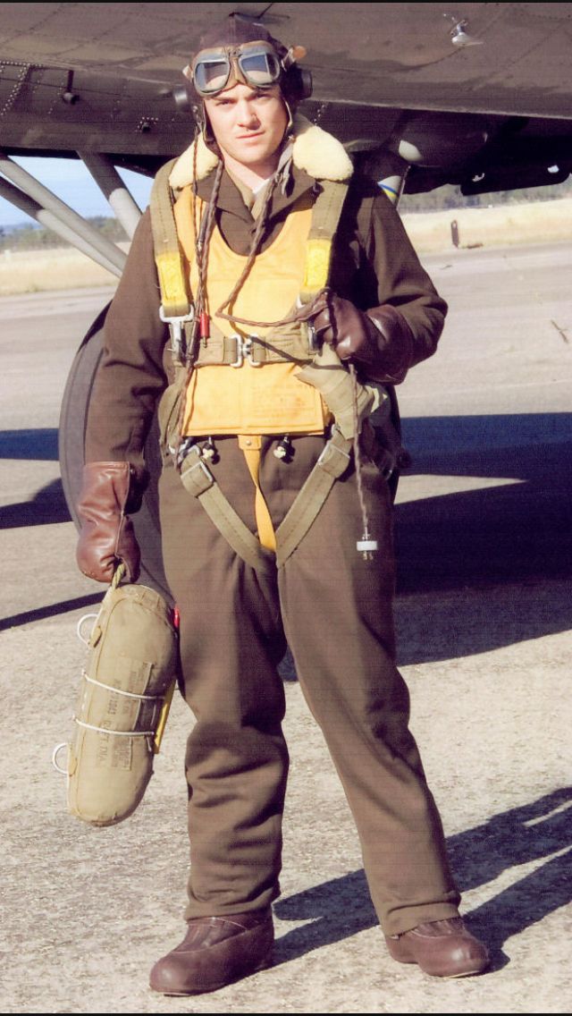 a man standing in front of an airplane with goggles on his head and holding a helmet