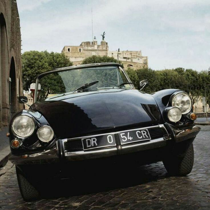 an old black car parked in front of a building on a cobblestone street