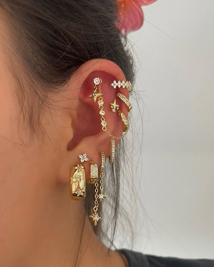 a woman wearing gold ear cuffs with cross and star charms