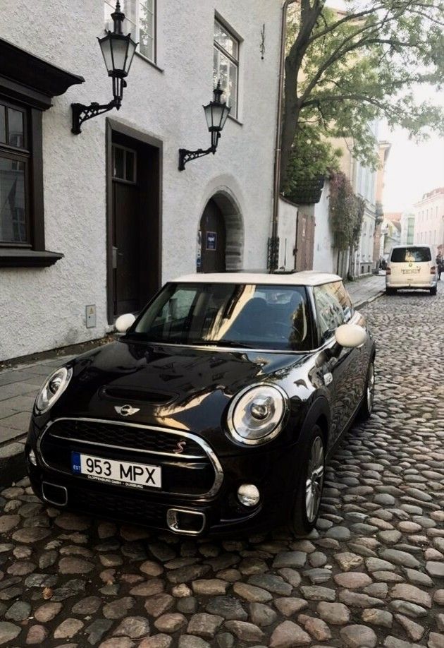 a small black car parked in front of a white building on a cobblestone street